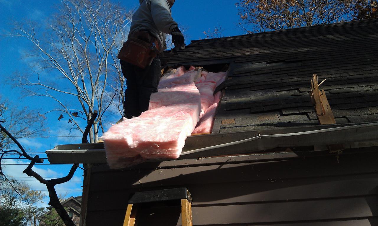 A man on a ladder putting insulation in the roof of a house.